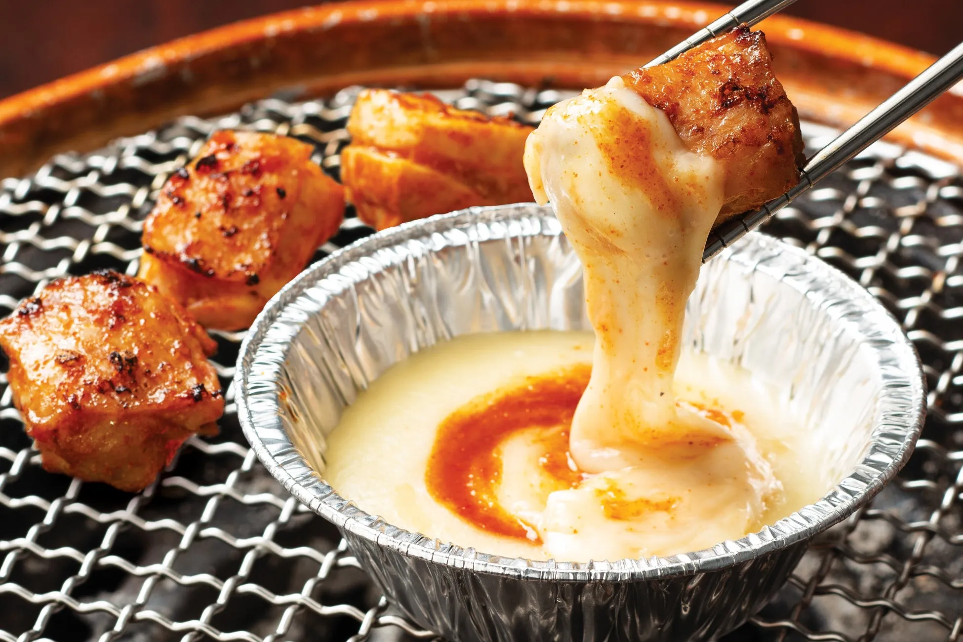 焼き肉とチーズフォンデュの様子を写した写真です。焼かれた肉がチーズフォンデュに浸され、美味しそうな光景が写されています。